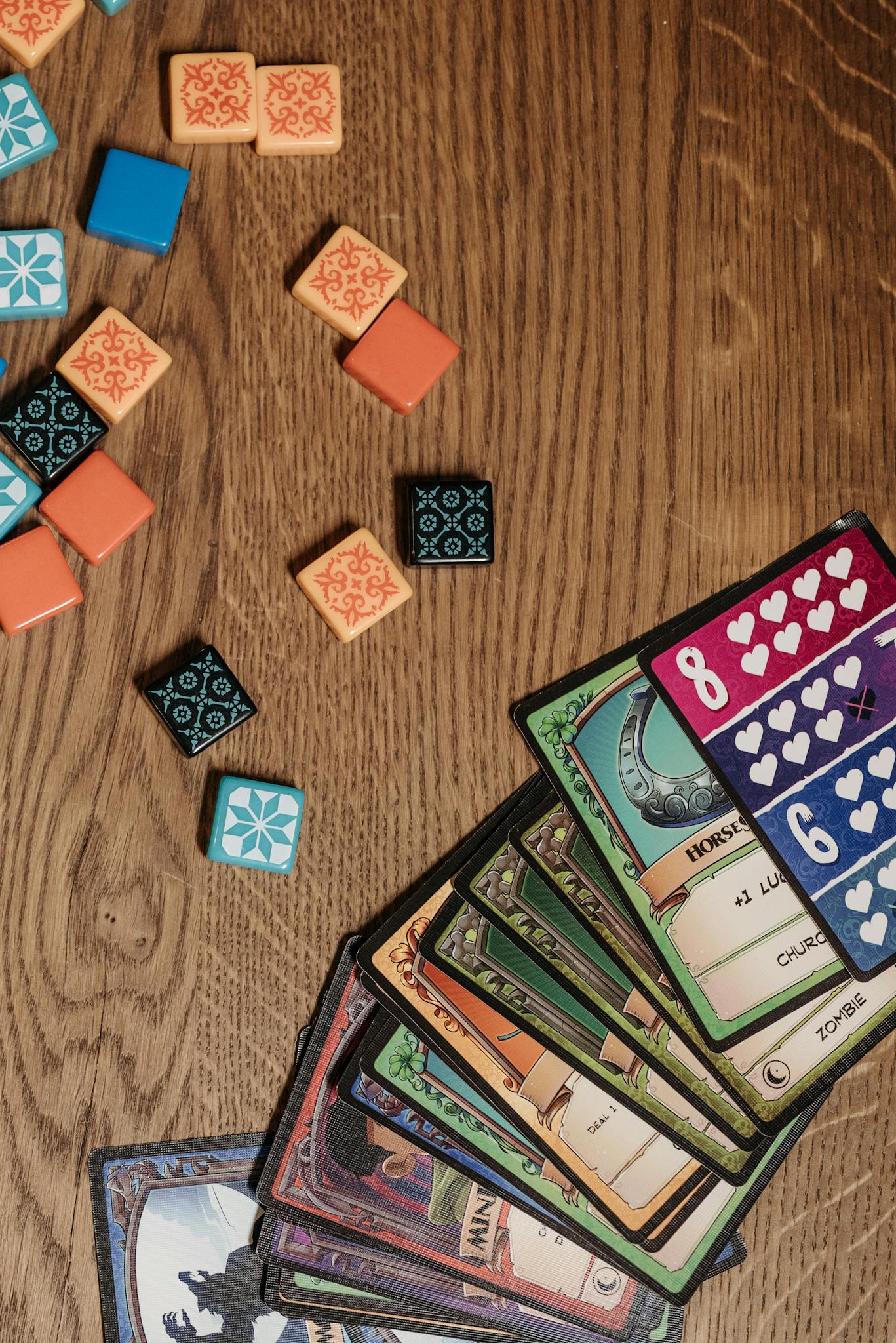 A variety of board game cards and tiles laid out on a wooden table, showcasing a fun and strategic gaming setup.